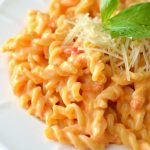 roasted red pepper macaroni and cheese on a white place with shredded parmesan and parsley garnish