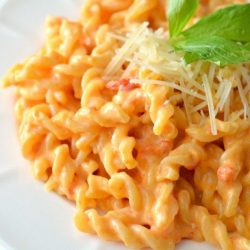 roasted red pepper macaroni and cheese on a white place with shredded parmesan and parsley garnish