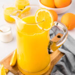 pitcher of fresh squeezed orange juice with oranges in the background.
