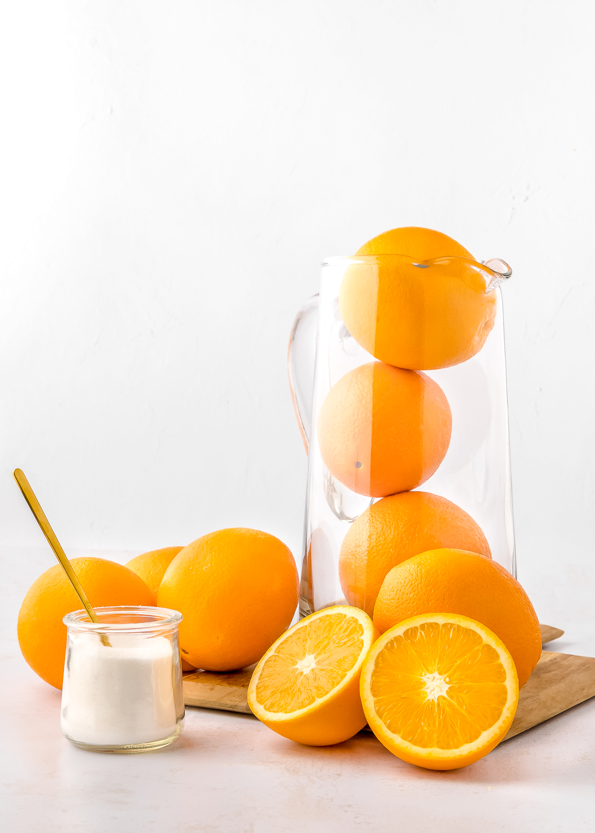 oranges in a pitcher, one cut in half and a small jar filled with sugar.