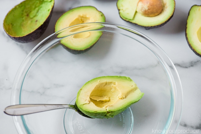 scooping avocado with a spoon for guacamole