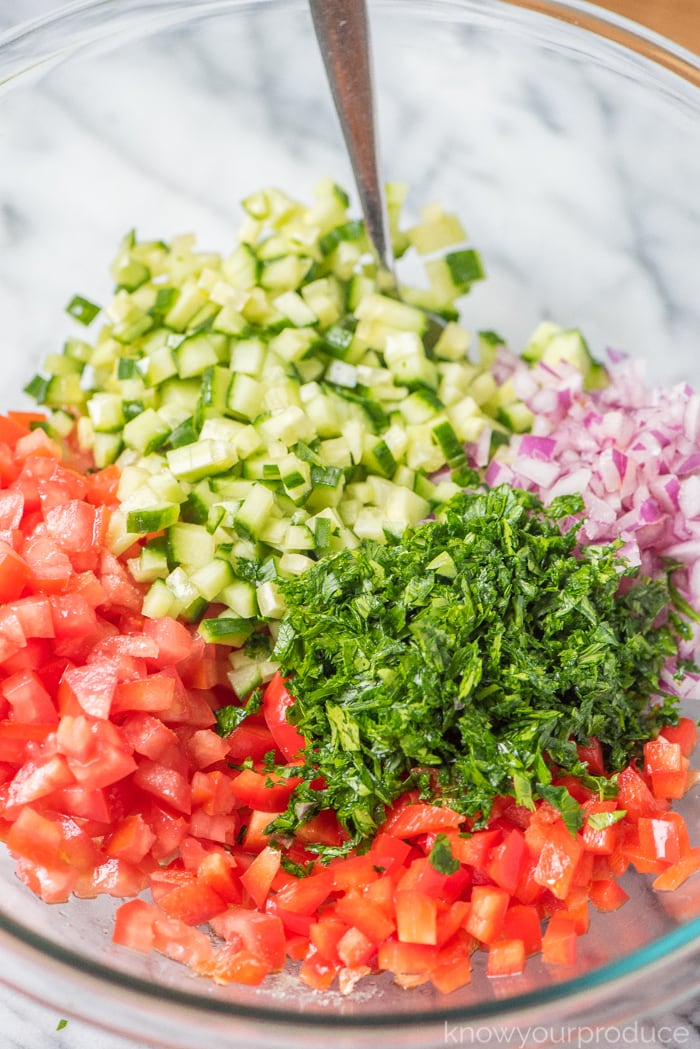 chopped vegetables and fresh herbs for Israeli salad in a large bowl