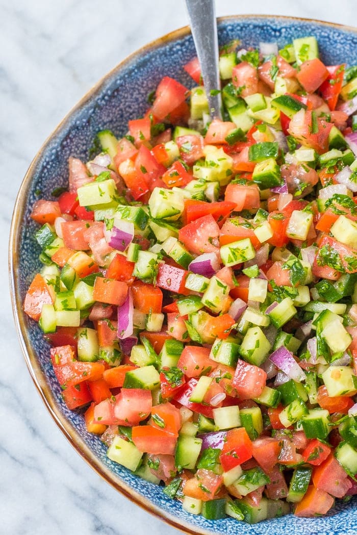 israeli salad in a blue bowl with spoon on top