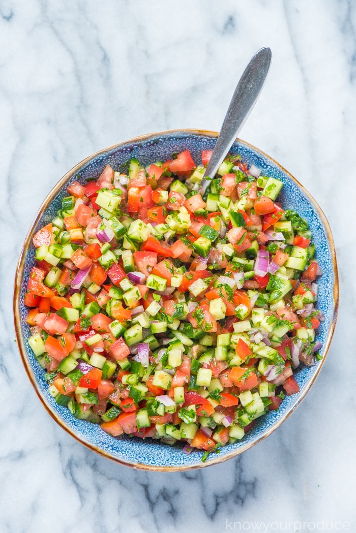 fresh chopped vegetable salad in a blue bowl with spoon