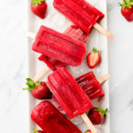 homemade strawberry popsicles on a tray with ice and halved strawberries.