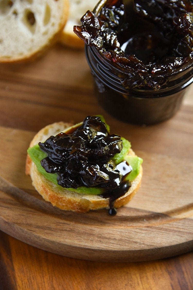 sweet balsamic onion relish on a piece of toast with avocado slices on a wooden cutting board