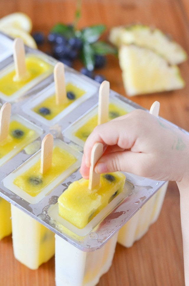 child's hand pulling out a pineapple lemonade popsicle with blueberries inside