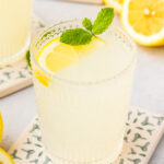 homemade lemonade in a glass cup with a lemon wedge and sprig of mint for color.
