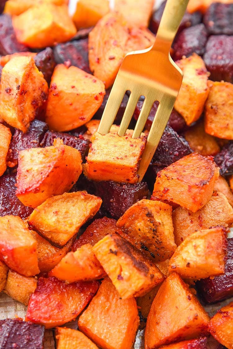 roasted beets and sweet potatoes on a sheet pan with a fork