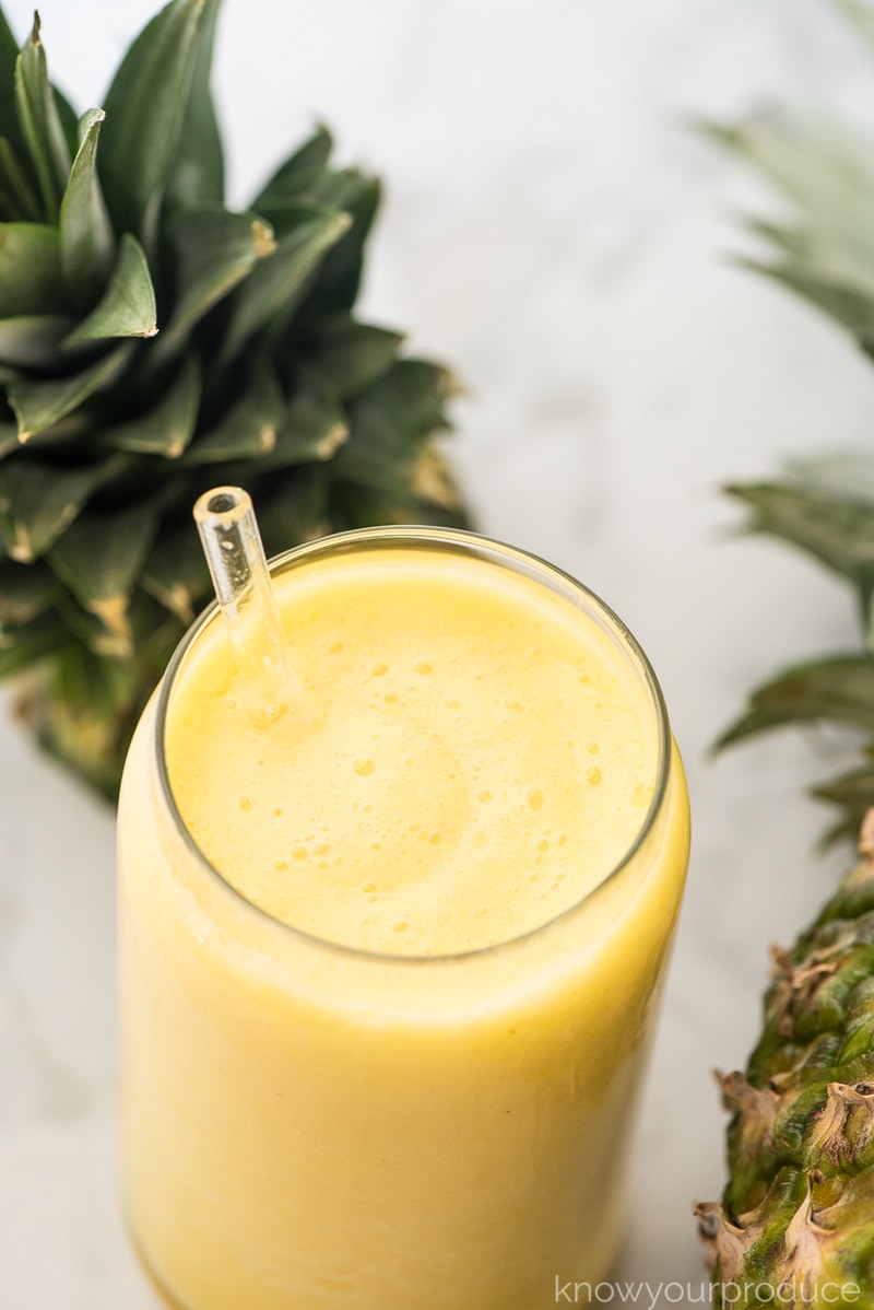 pineapple lemonade in a glass with a glass straw and pineapples on the side