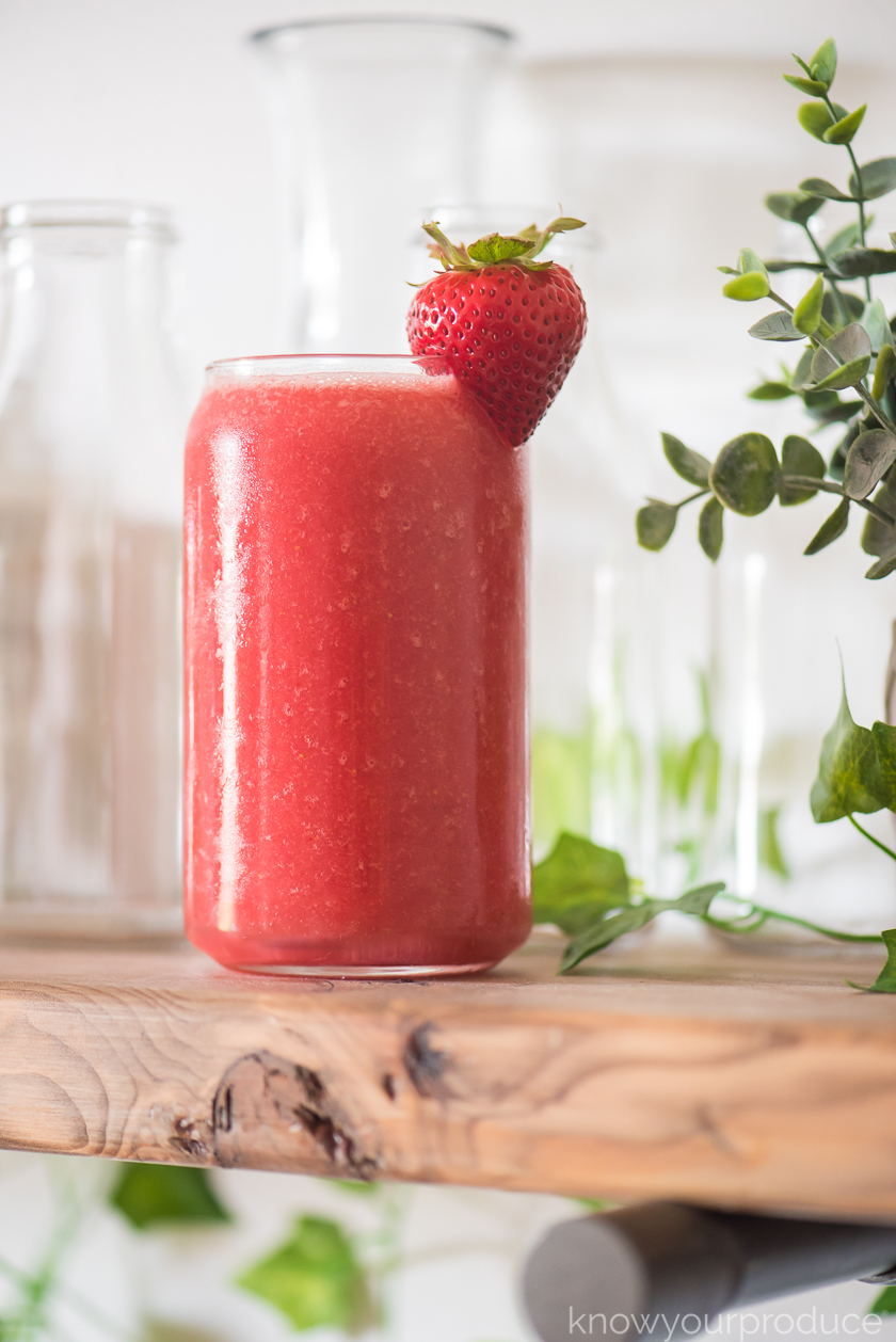 strawberry watermelon juice in a glass cup on a rustic shelf with empty glass jars and greenery around