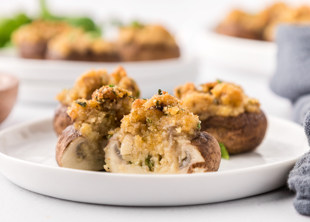 stuffed mushrooms on a plate with the front one sliced in half to show the inside.