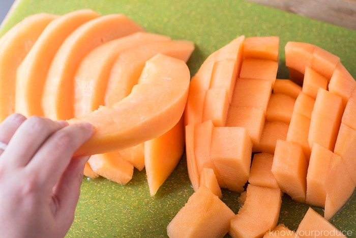 hand grabbing slice of cantaloupe on a green cutting board