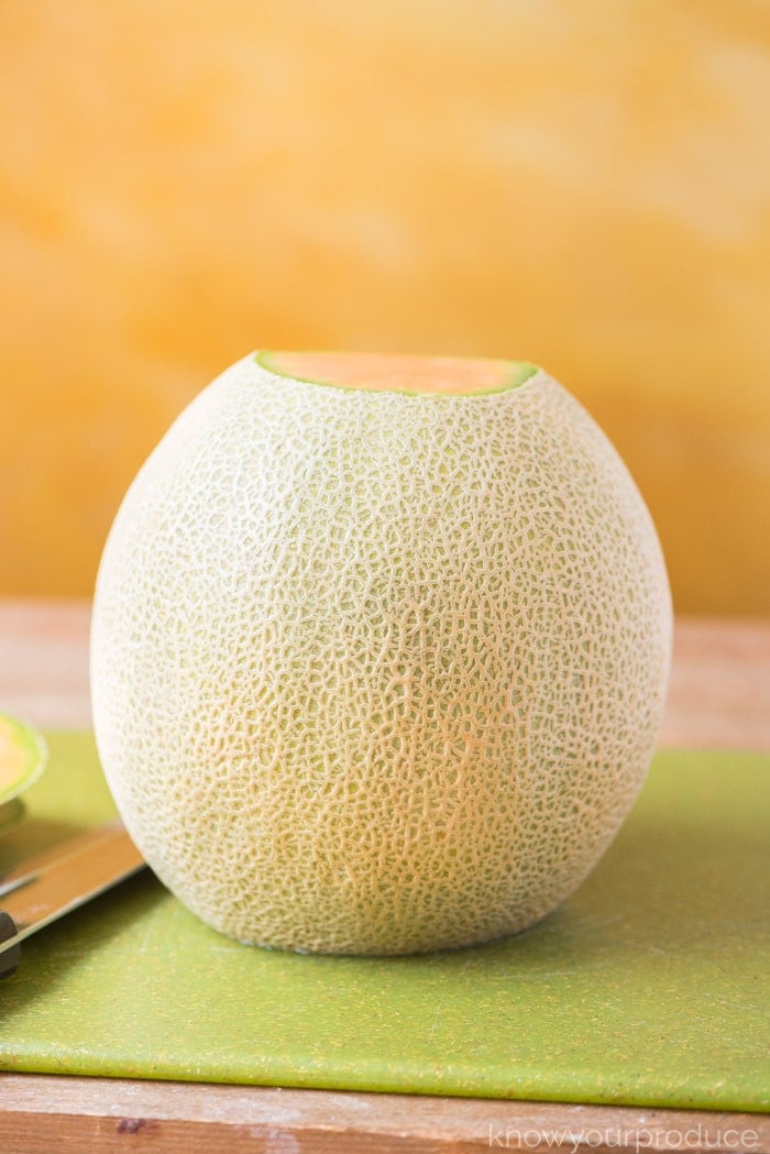 cantaloupe standing on cutting board with bottom and top sliced off 