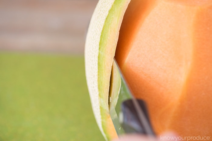 closeup of knife cutting off cantaloupe rind