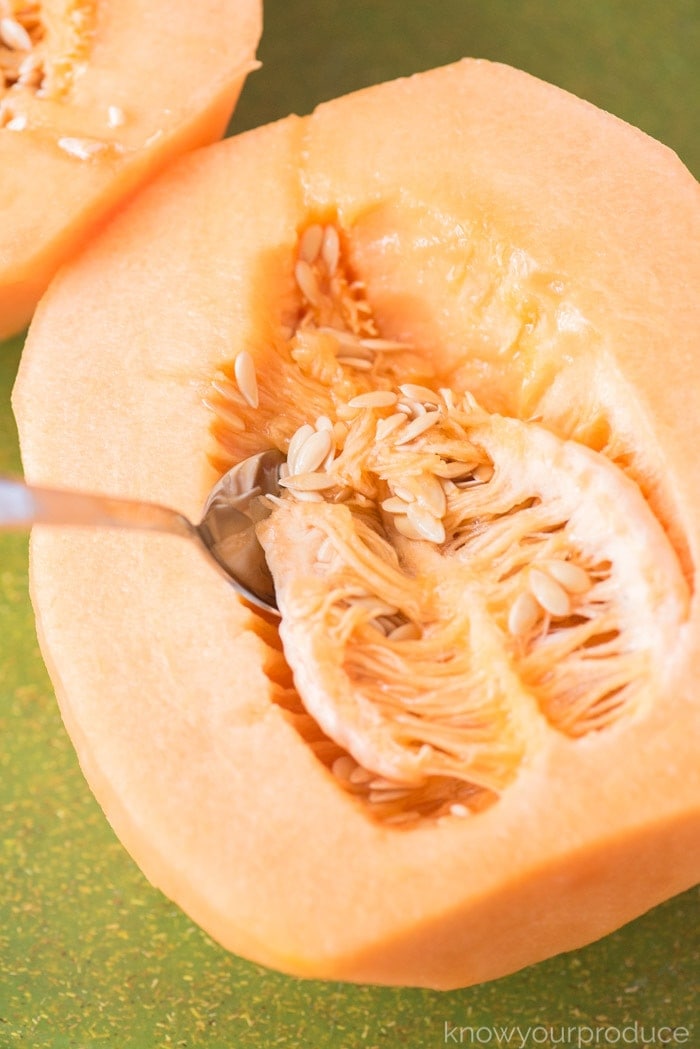 half of cantaloupe on a cutting board with spoon inside scooping out cantaloupe seeds