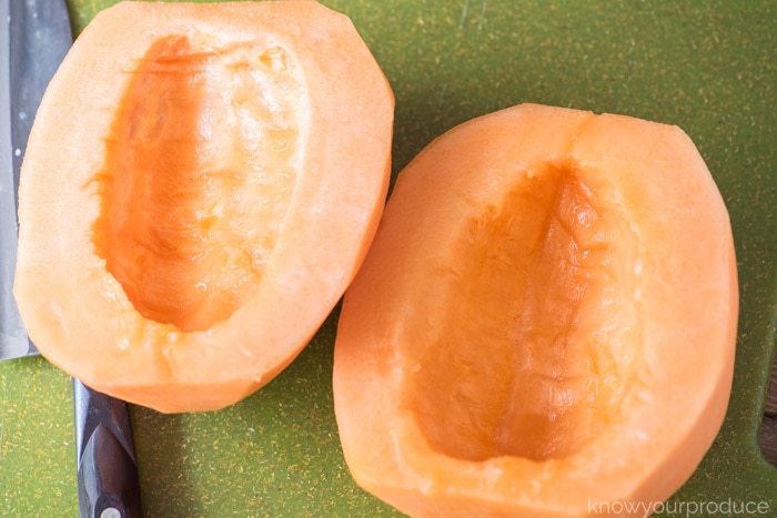 two halves of cantaloupe on a green cutting board with seeds removed