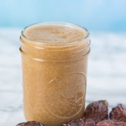 date syrup in a small mason jar with fresh dates on a marble board