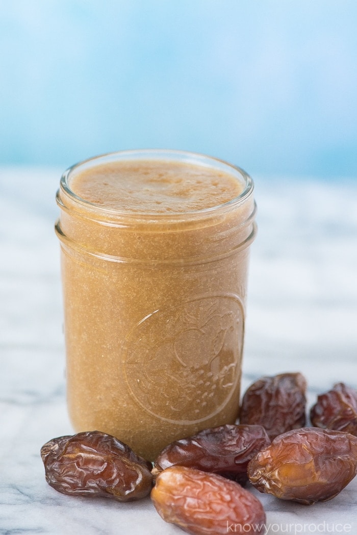 date syrup in a small mason jar with fresh dates on a marble board