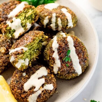 homemade falafel on a platter with tahini sauce drizzled on it.