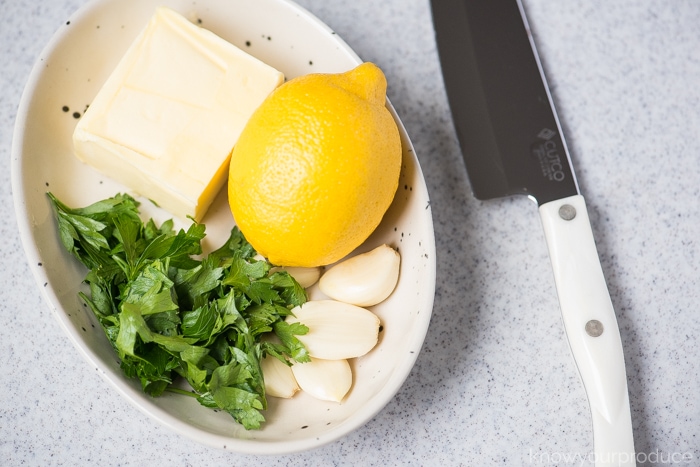 ingredients for lemon garlic butter sauce in a bowl on a cutting board with a santoku knife