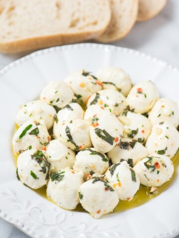 marinated mozzarella balls on a plate with crusty bread on a marble pastry board