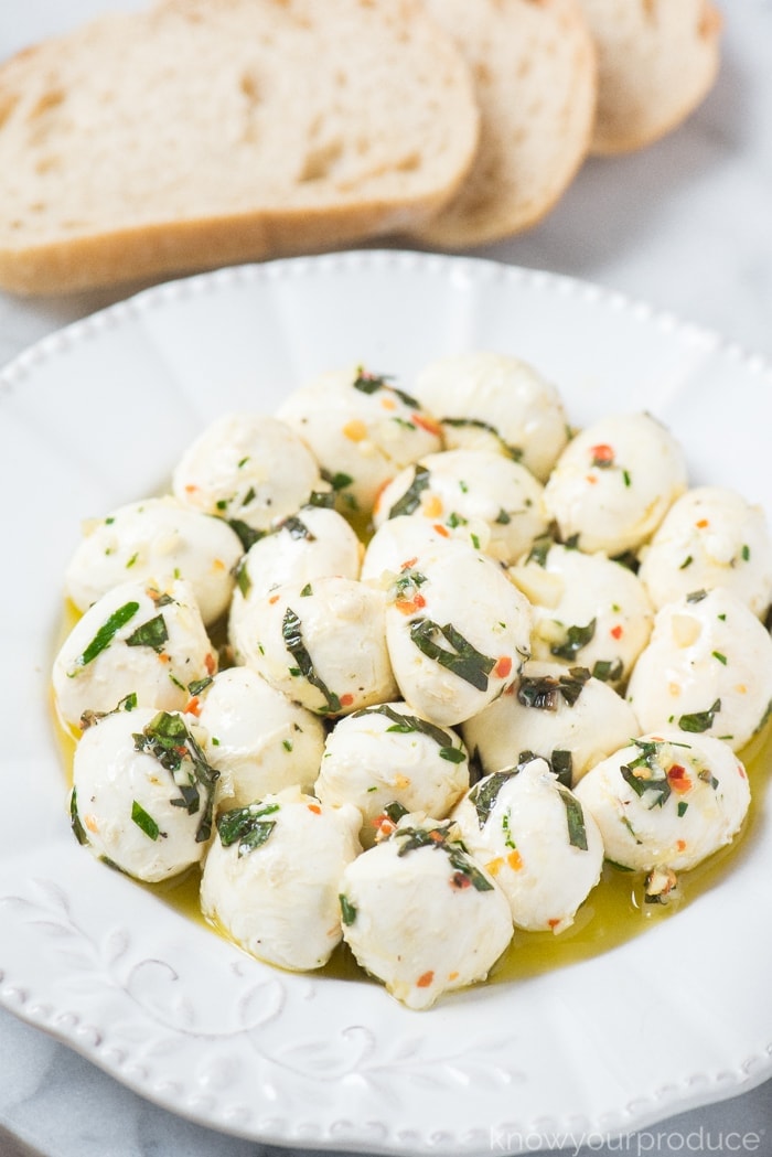 marinated mozzarella balls on a plate with crusty bread on a marble pastry board