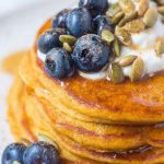 pumpkin pancakes covered in syrup on a plate with blueberries sunflower seeds and greek yogurt