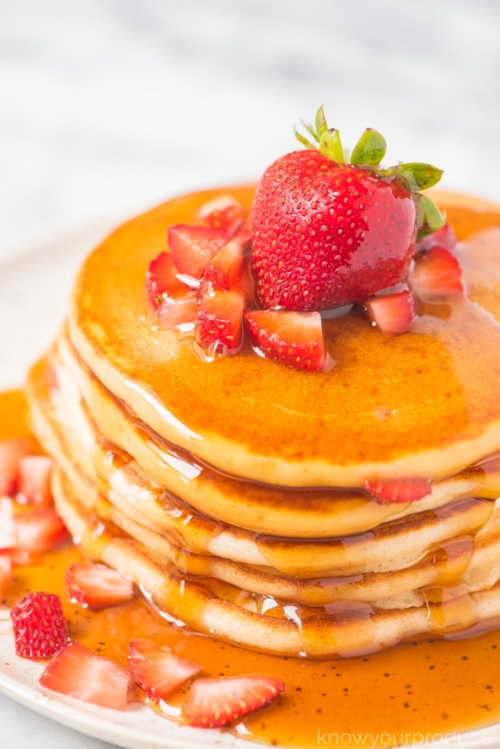 strawberry pancakes covered in maple syrup on a plate