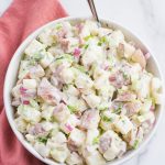 vegan potato salad in a white bowl with a spoon and pink napkin