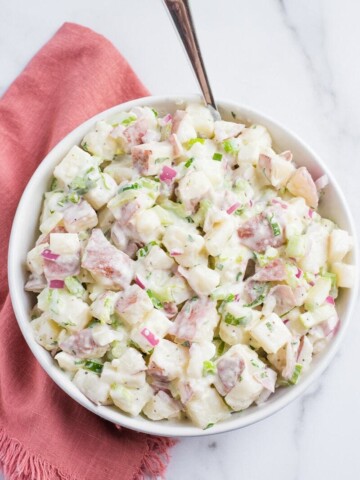 vegan potato salad in a white bowl with a spoon and pink napkin