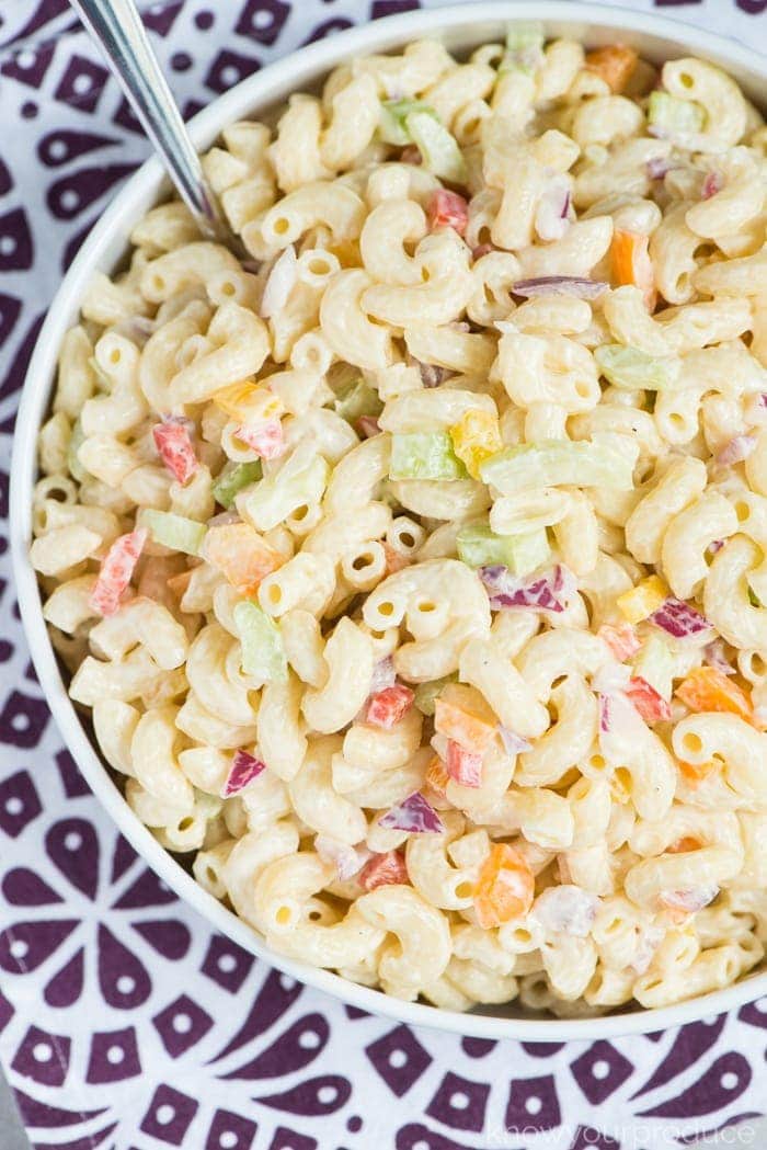 vegan macaroni salad in a low bowl with a spoon on a purple and white napkin