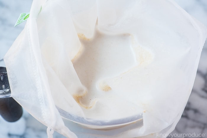 straining oat milk in a nut milk bag