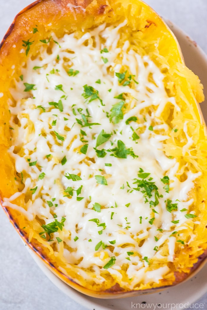 cooked spaghetti squash boat with melted mozzarella cheese and chopped parsley in a bowl