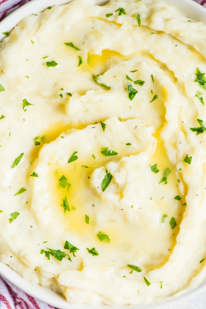 vegan mashed potatoes in a low bowl swirled with melted butter and parsley garnish