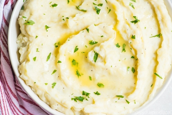 vegan mashed potatoes in a low bowl swirled with butter and parsley garnish with a white and red striped napkin to the left