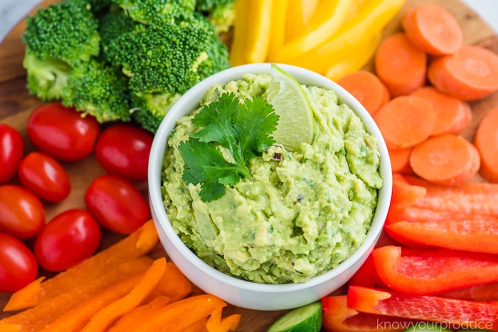 guacamole in a bowl with lime wedge and cilantro garnish in middle of vegetable platter 