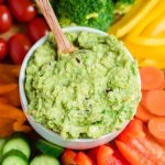 guacamole in a bowl with wooden spoon in middle of vegetable platter