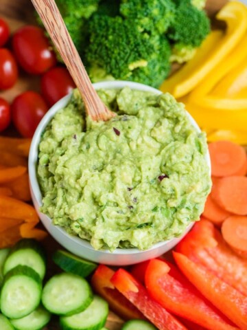 guacamole in a bowl with wooden spoon in middle of vegetable platter