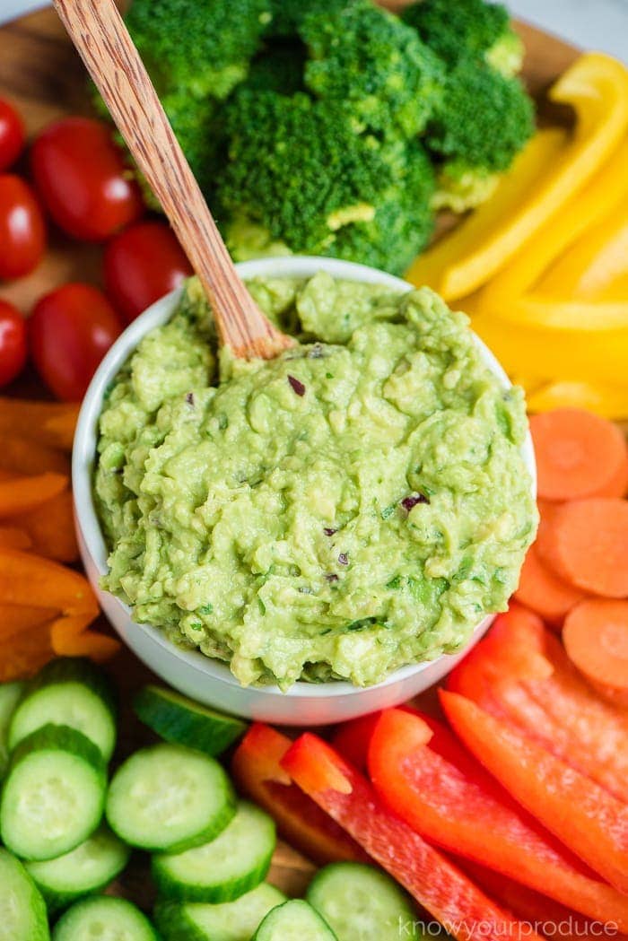 guacamole in a bowl with wooden spoon in middle of vegetable platter