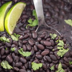 instant pot black beans with stainless steel spoon inside and garnished with lime and cilantro