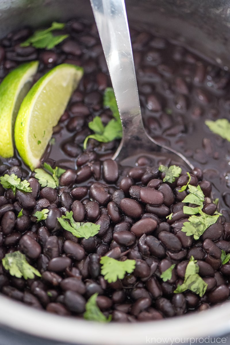 instant pot black beans with stainless steel spoon inside and garnished with lime and cilantro