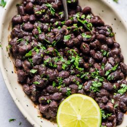 mexican black beans in bowl with spoon, lime wedge, and cilantro garnish