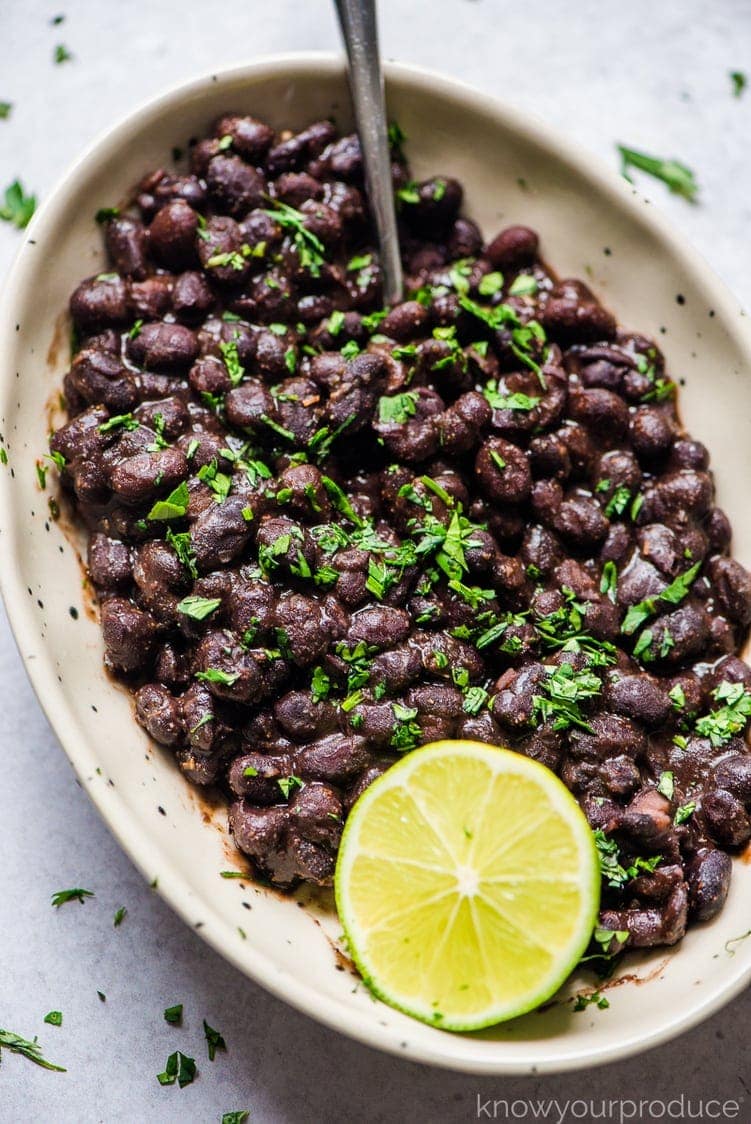 mexican black beans in bowl with spoon, lime wedge, and cilantro garnish