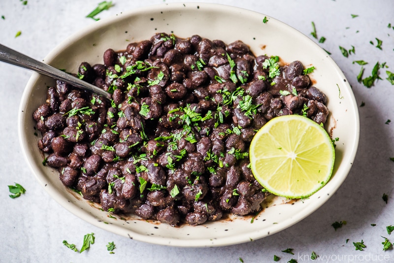 mexican black beans in bowl with lime wedge and cilantro garnish and spoon to the side