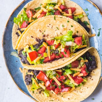 vegan tacos with black beans, lettuce, vegan cheese shreds, and fresh pico de gallo on a blue plate