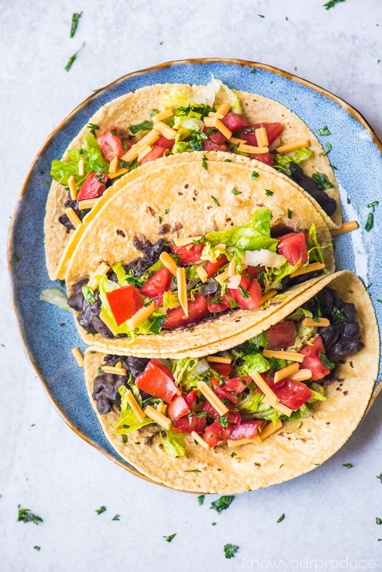 vegan tacos with black beans, lettuce, vegan cheese shreds, and fresh pico de gallo on a blue plate