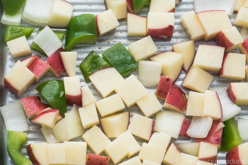 raw potatoes peppers and onions on a sheet pan