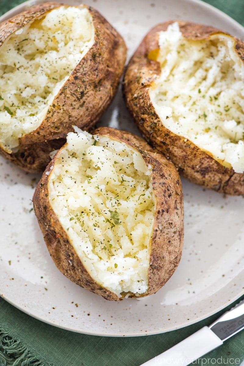 seasoned and buttered baked potatoes fork mashed on a plate with a knife on a green napkin