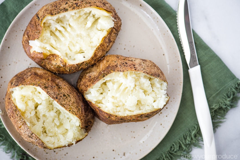 baked potatoes on a plate with a knife to the side on a green napkin